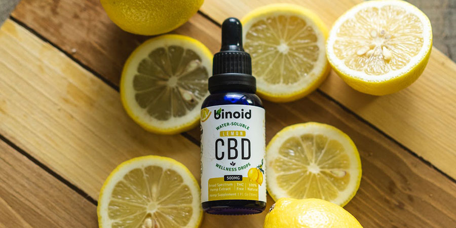 a small bottle of CBD oil surrounded by sliced and whole lemons on top of a wooden chopping board